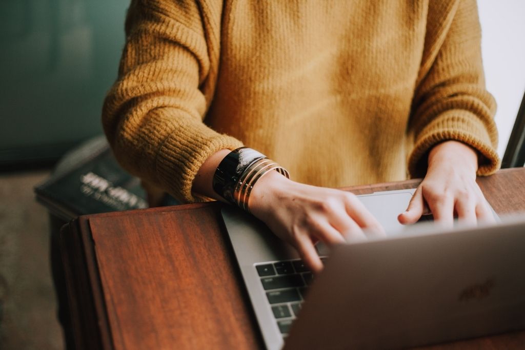 A graduate student in an orange sweater takes classes online with a laptop