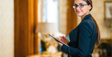 A woman with glasses holding a tablet while checking guests into their hotel room