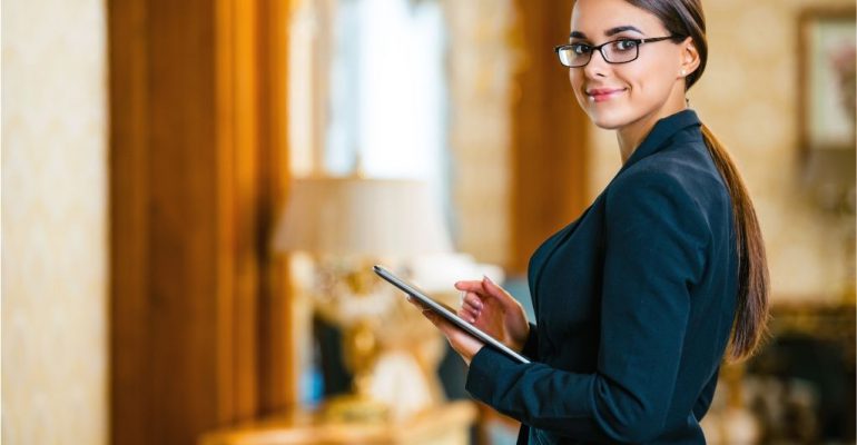 A woman with glasses holding a tablet while checking guests into their hotel room