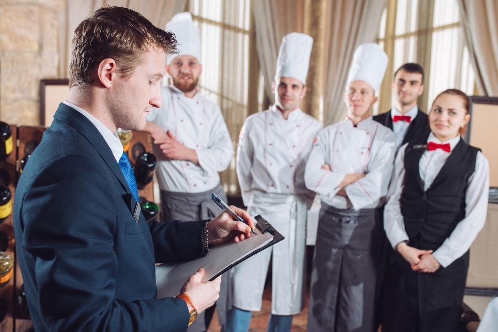 A male food and beverage manager oversees chefs and wait staff