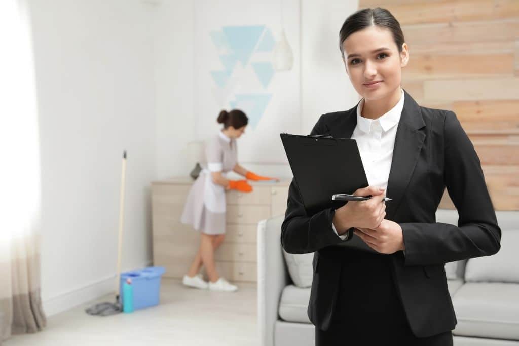 A female Director of Housekeeping watches over a maid clean a hotel room