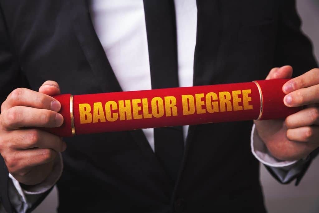 Man in a suit holding a red tube that says bachelor degree on it.