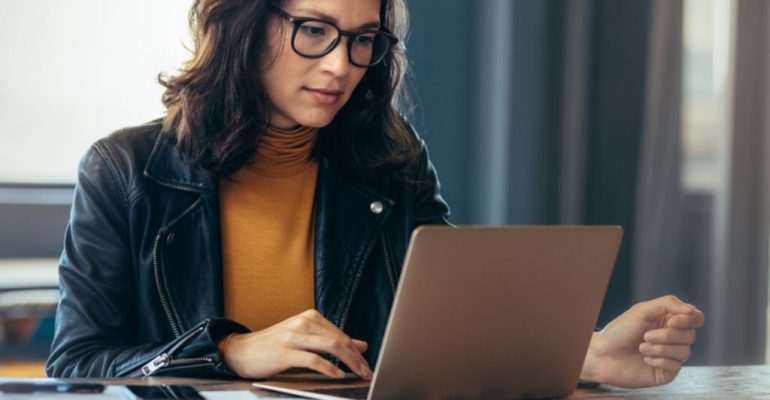 Woman working on a laptop with papers around her.