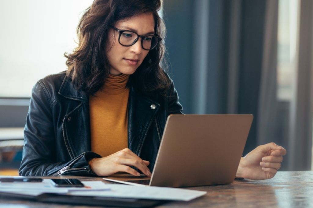 Woman working on a laptop with papers around her.