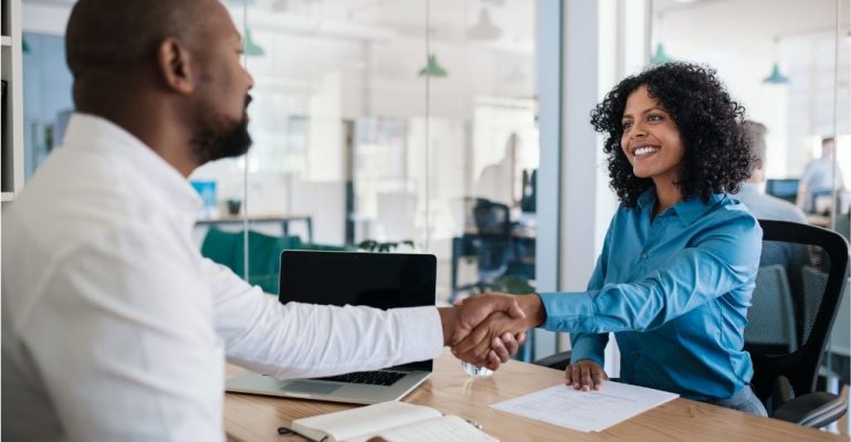 A male HR manager shakes the hand of a smiling female employee