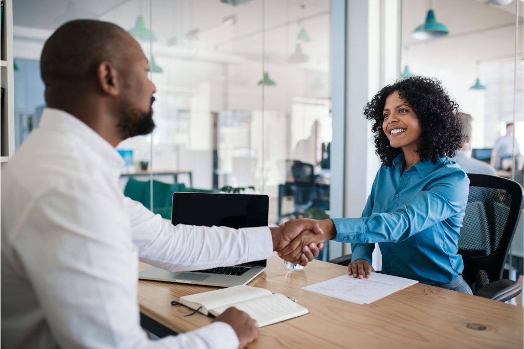 A male HR manager shakes the hand of a smiling female employee