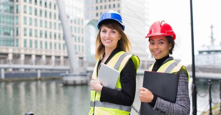 Two female construction management students hold tablets while working on a job site.