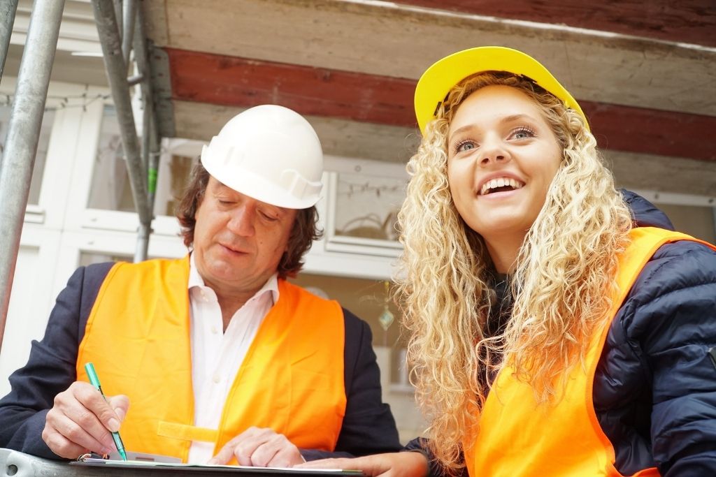 An older male construction manager works with a young female student on the job site