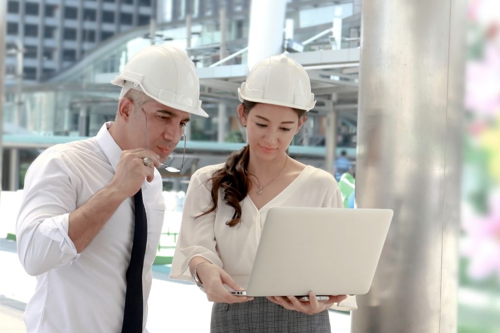 Man and woman in hardhats looking at a laptop on a construction site.