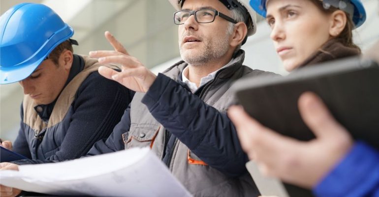 Man leading two individuals on a construction site.