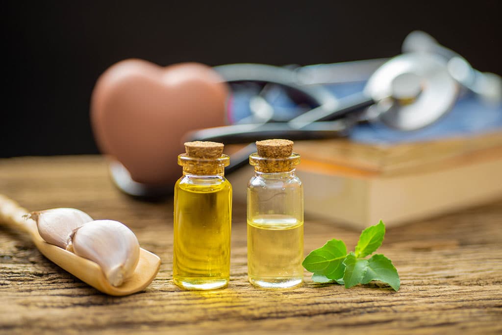 Oils, garlic, and herbs next to a textbook on a table.