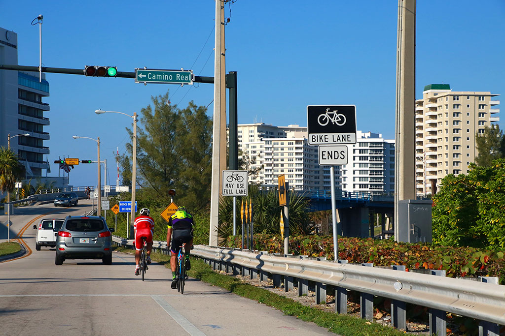 Two men cycle behind a car in Boca Raton