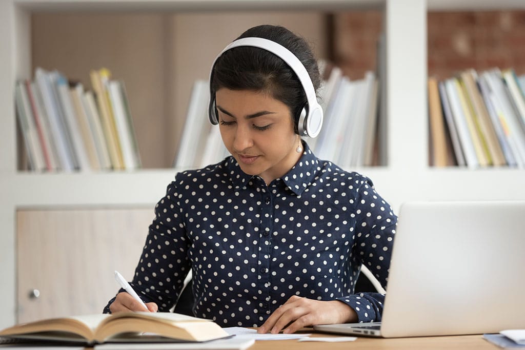 Female college student listens to an online course in front of a laptop