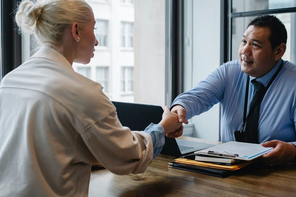 An older male human resource manager shakes hands with a young female at a job interview.