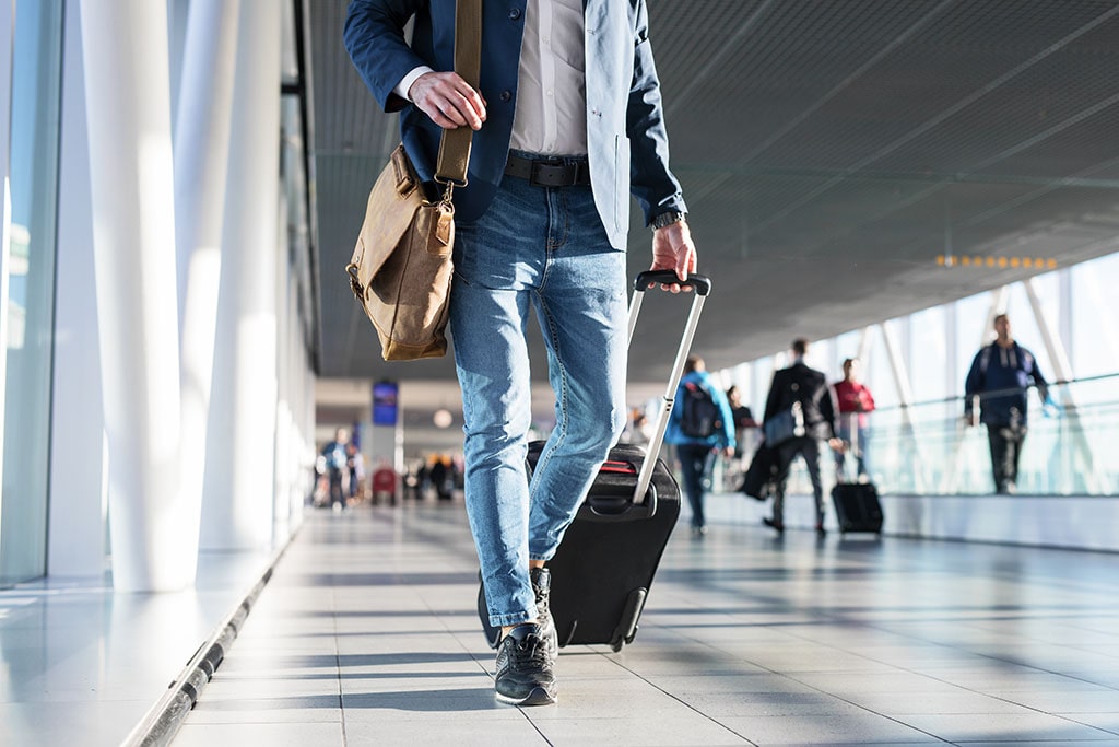 Man walking through the airport with his suitcase and several other travelers in the background.