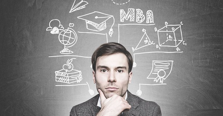 A young man stands in front of a chalkboard with ideas about what you can do with an MBA.