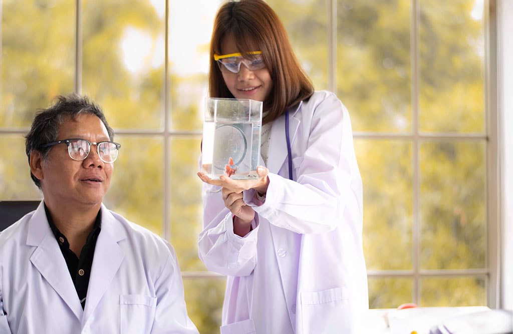 An older male professor talks with a young female student about a fish in a small tank