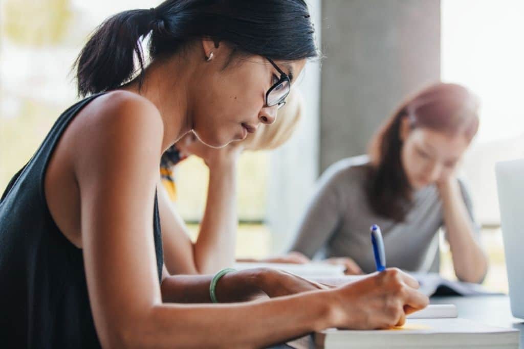 College students writing notes on paper in a library.