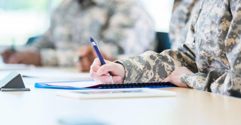 Student writing with man in background in military friendly colleges