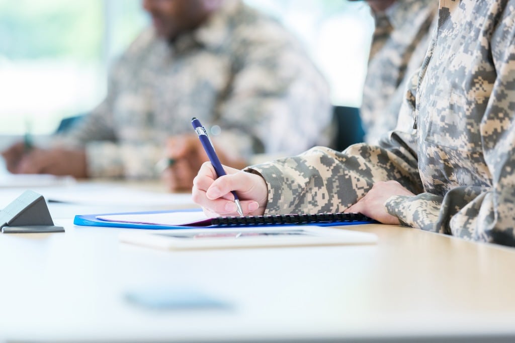 Student writing with man in background in military friendly colleges