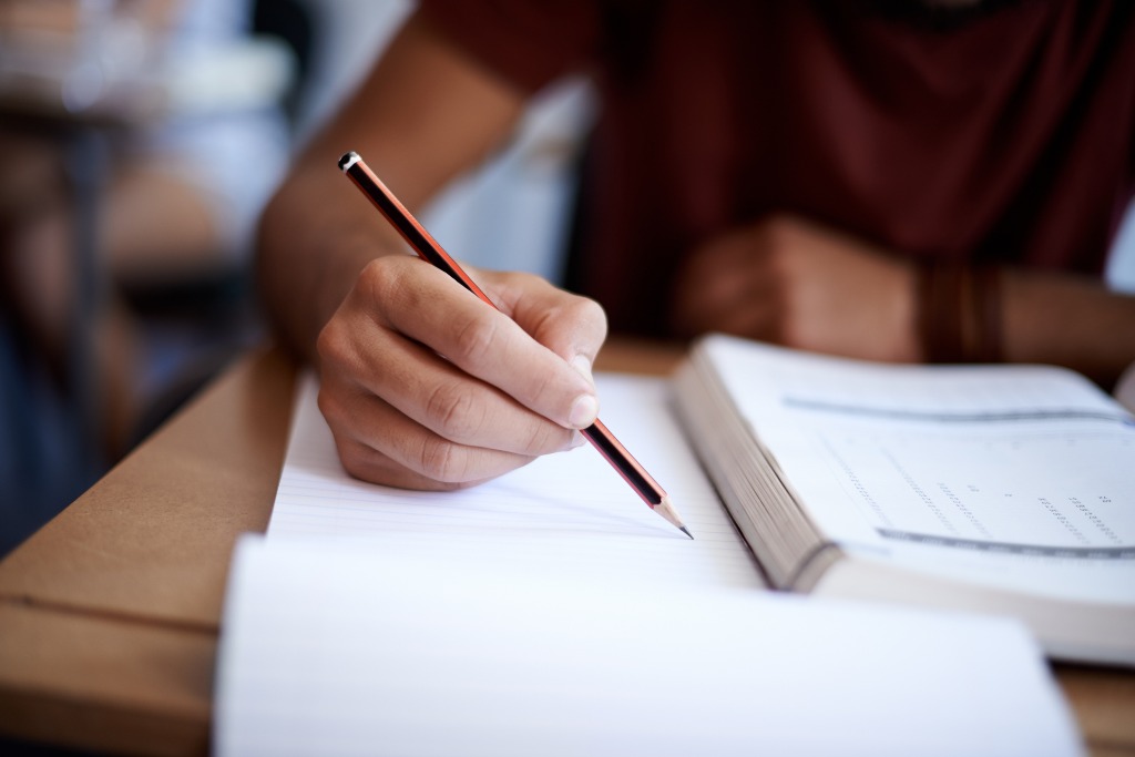 A Student writing notes while studying with their textbook