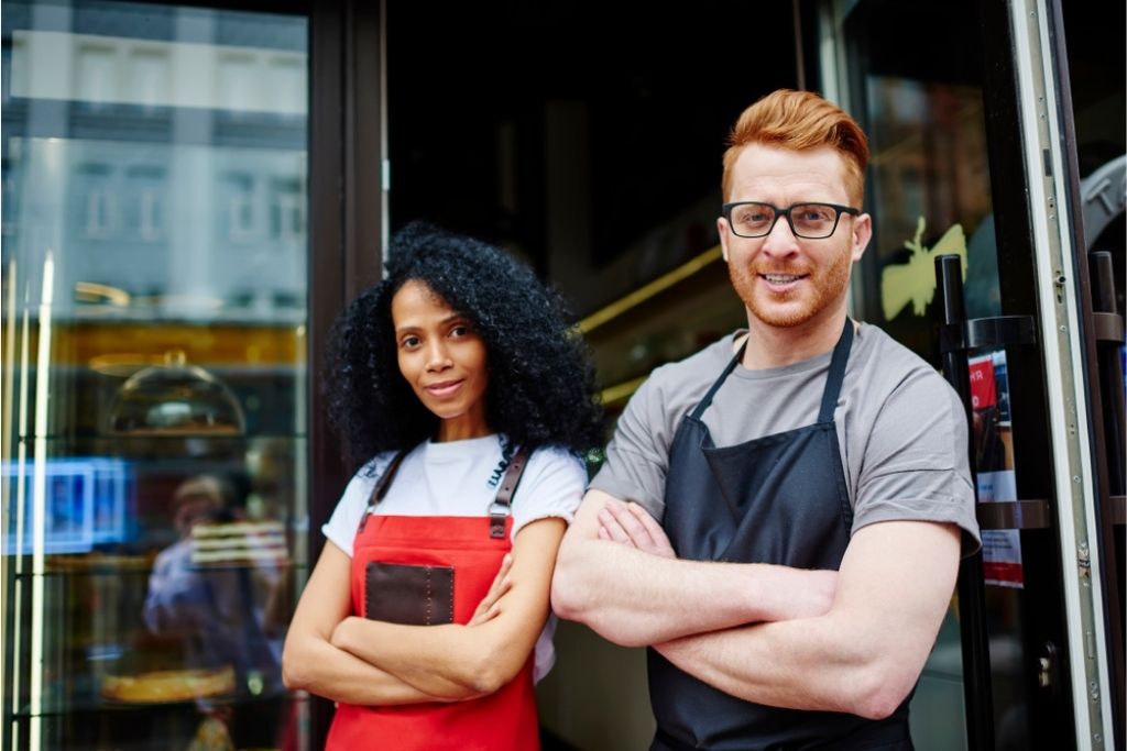 Owners of a restaurant standing outside their establishment smiling.