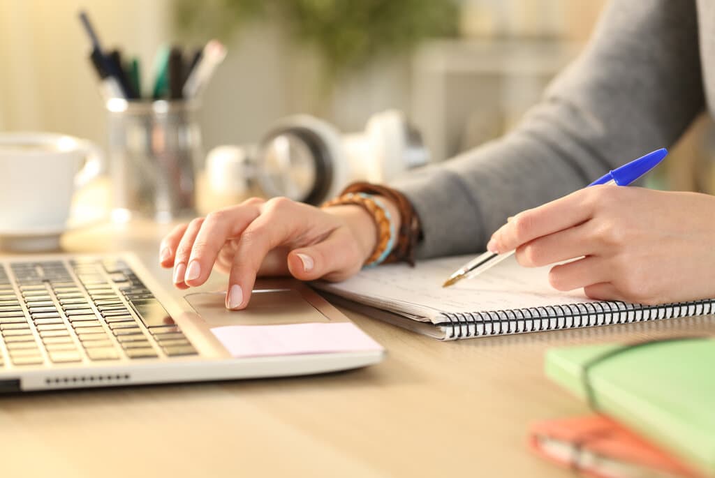 A woman studying with a laptop, notebook, and cup on the table.