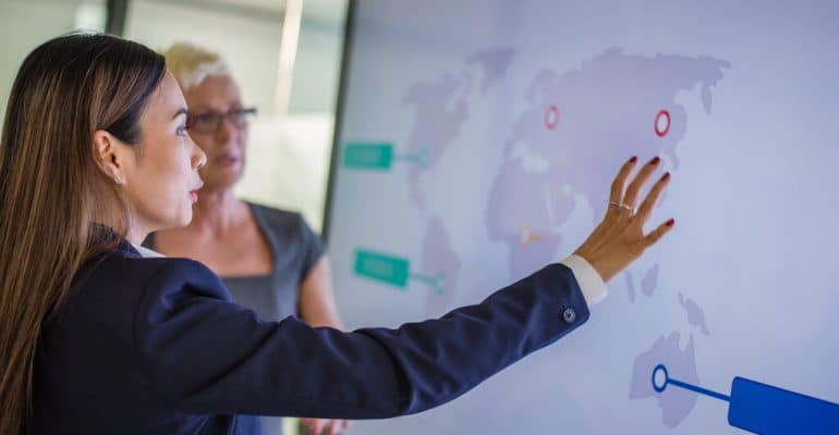 A woman doing a business presentation with a screen showing a map of the world.