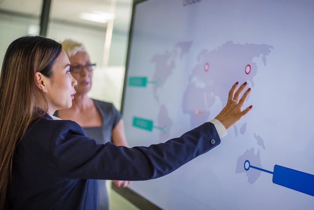 A woman doing a business presentation with a screen showing a map of the world.