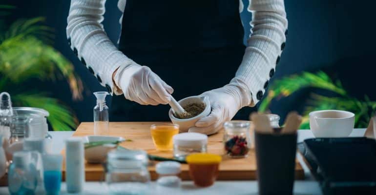 Hands grinding herbs with a mortar and pestle beside bowls of natural remedies and tea