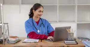 Public health professional in scrubs working on a laptop at a desk