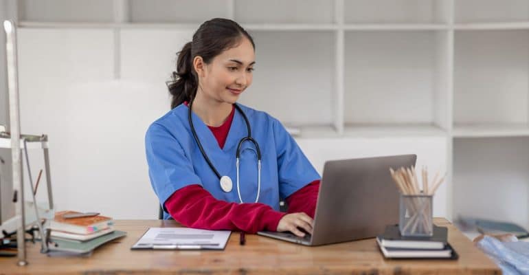 Public health professional in scrubs working on a laptop at a desk