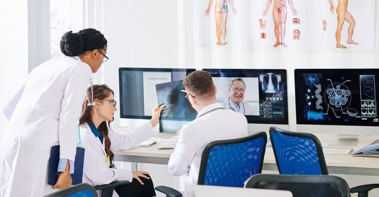 Clinicians reviewing medical scans on multiple screens in a diagnostics room