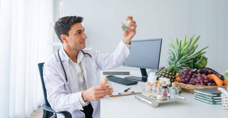 Healthcare professional in a white coat at a desk with fresh fruit and study materials