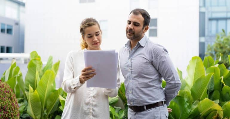 Two professionals reviewing a document outdoors surrounded by greenery