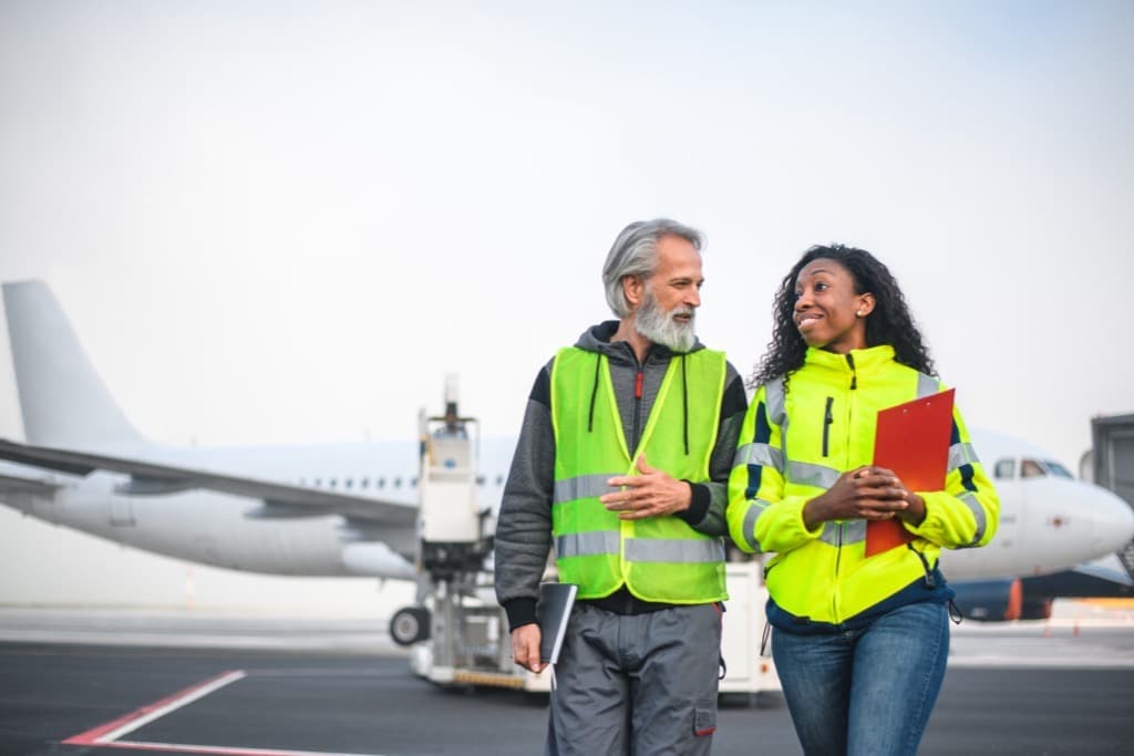 Airport ground crew member in a safety vest and headset inspecting a service panel under an aircraft