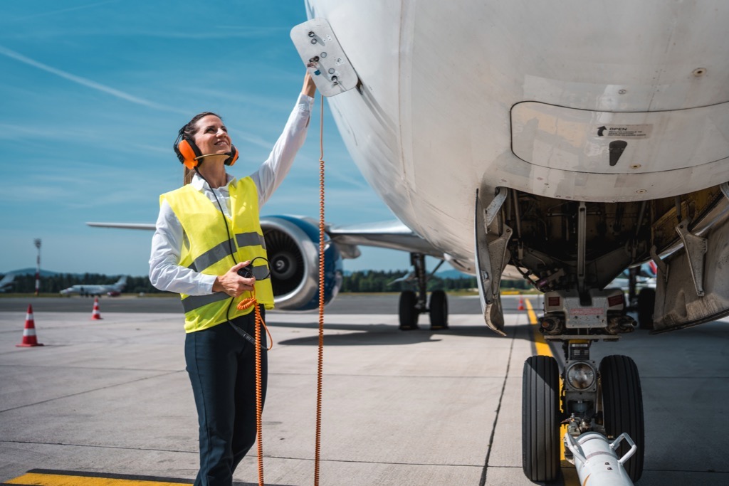 Two aviation ground crew in hi-vis gear walking and talking on the tarmac in front of a passenger jet