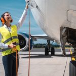 Two aviation ground crew in hi-vis gear walking and talking on the tarmac in front of a passenger jet