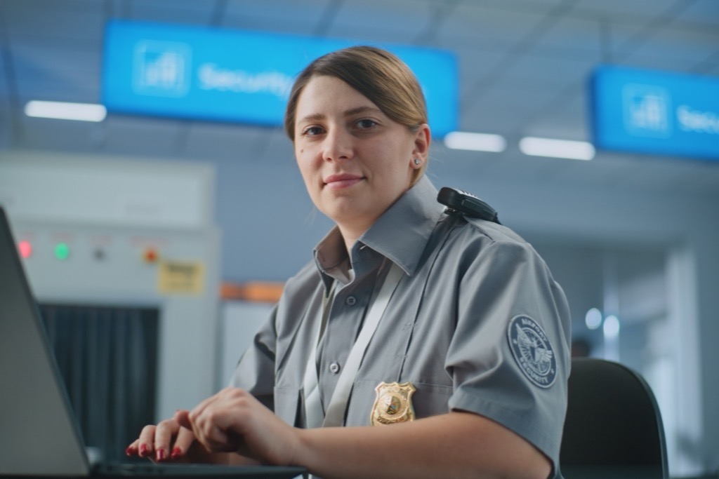 Airport security officer in uniform with a badge working at a laptop beside a checkpoint scanner