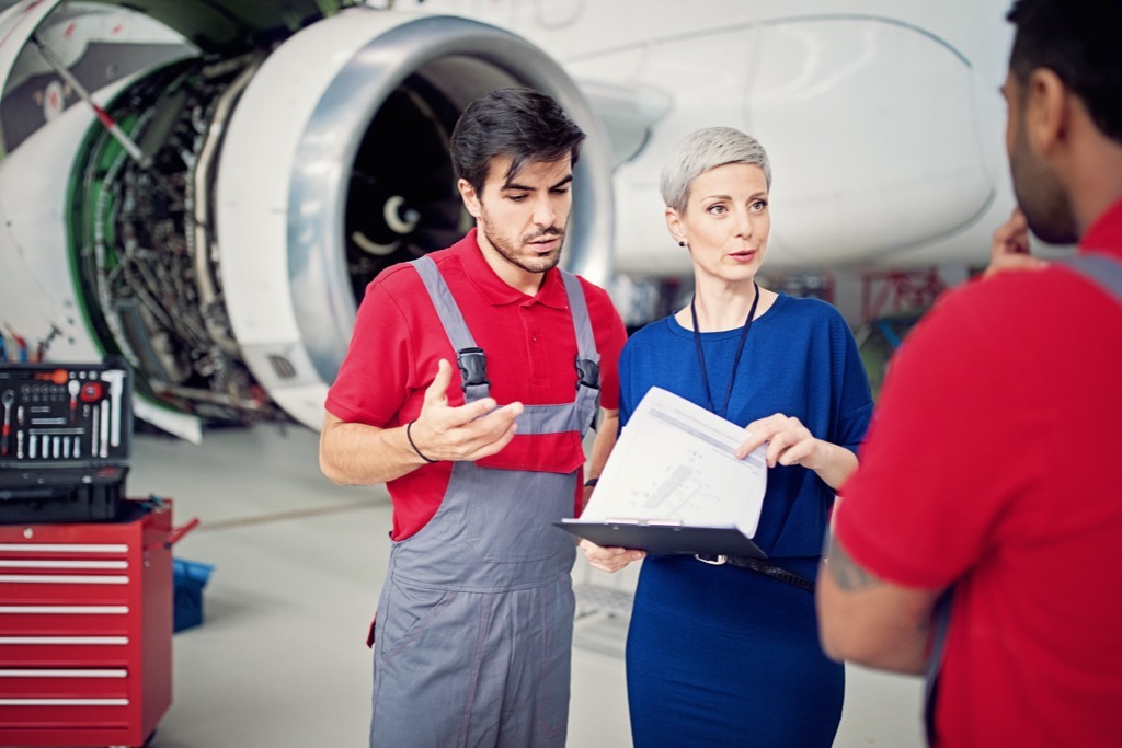 Aircraft maintenance manager reviewing documents with two mechanics beside an open jet engine