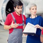Aircraft maintenance manager reviewing documents with two mechanics beside an open jet engine