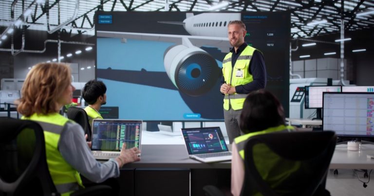Instructor in a safety vest leading an aviation team meeting with an aircraft engine on a large screen